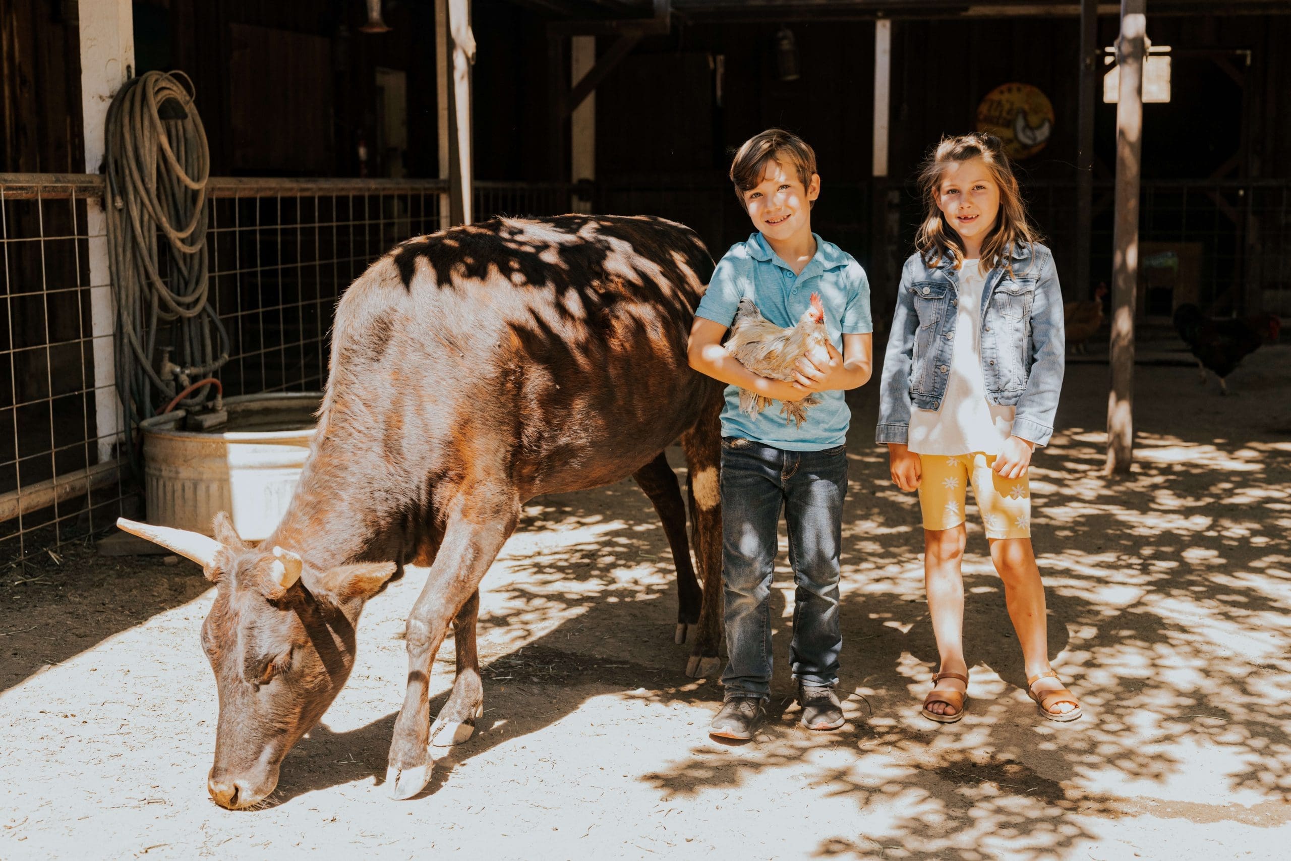 two young people posing with a chicken and calf