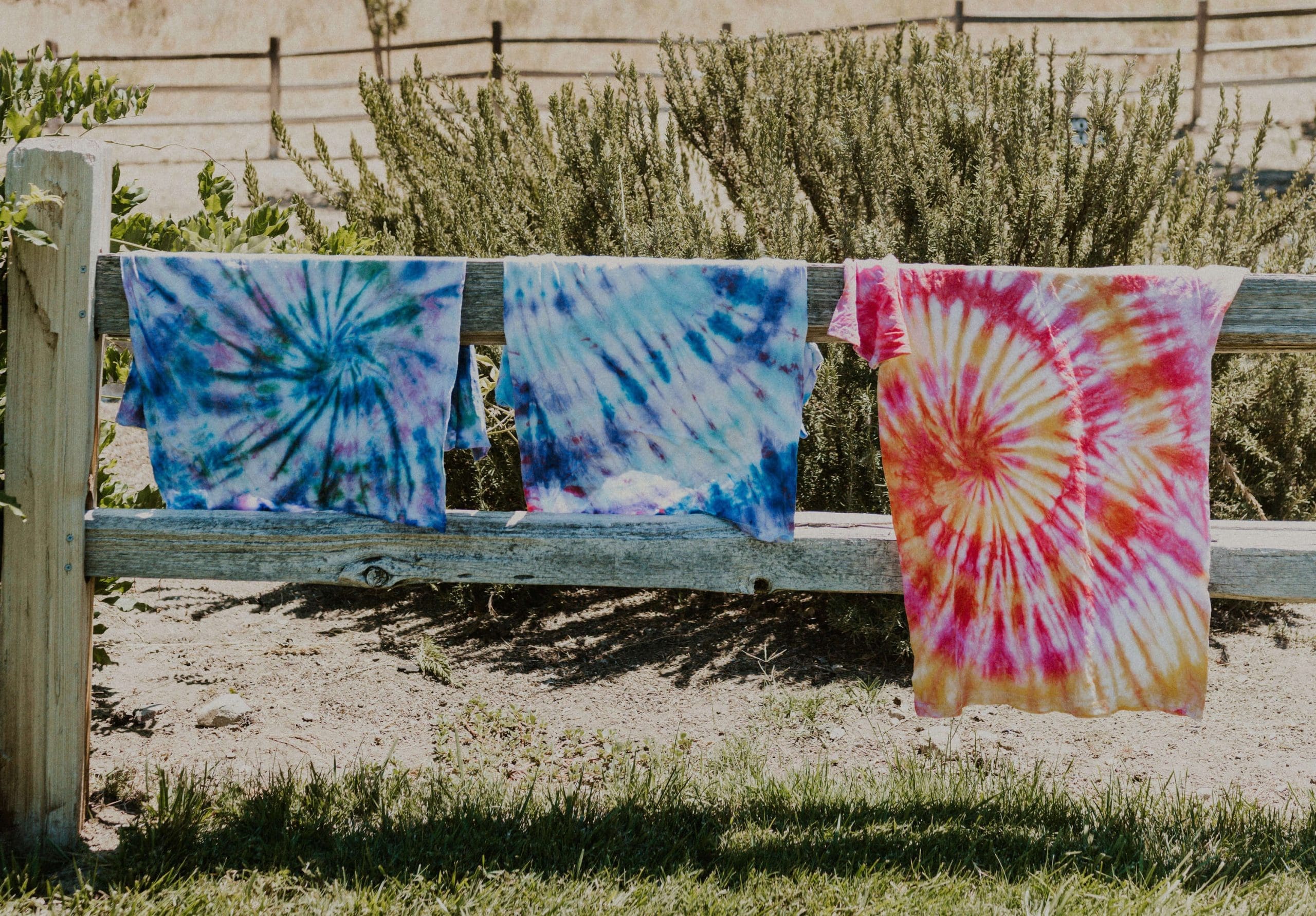 tie dyed t-shirts hanging on a fence